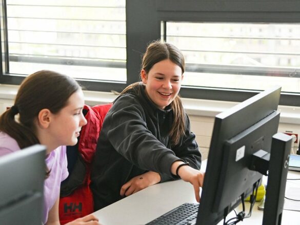 FH_GD_2023-pcgruppe Zwei Mädchen sitzen lachend vor einem PC-Bildschirm.