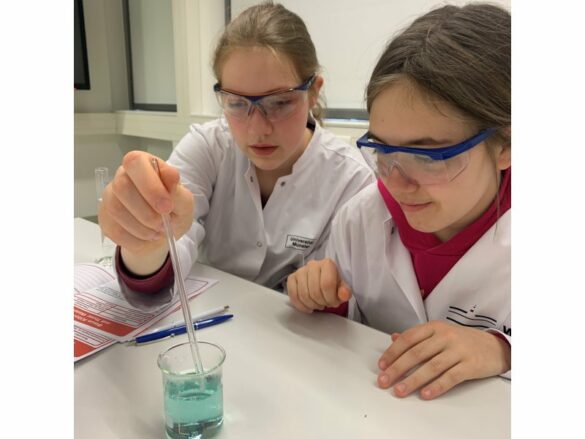 wwu-chemie-8 Zwei Mädchen geben mit einer Pipette ein paar Tropfen in ein Glas, das sich grün verfärbt hat.