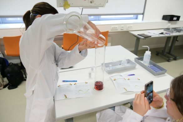 Chemische Ampel Die Mädchen füllen verschieden farbige Flüssigkeiten in einen Zylinder