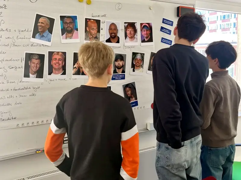 BoysDay-amt-17-2026-2 Drei Jungen stehen vor einer Moderationswand und diskutieren verschiedene Männlichkeitstypen, die als Fotos aufgehängt sind.