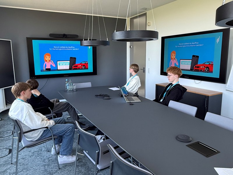 Boysday-2026-ECON-TEL-1 Drei Jungen sitzen in einem Konferenzraum vor einem großen Screen.
