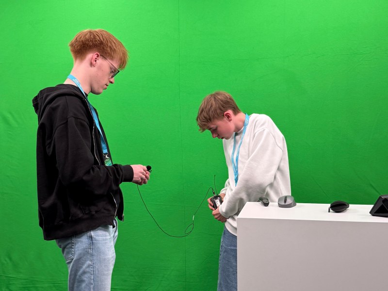 Boysday-2026-ECON-TEL-2 Zwei Jungen bereiten sich für eine Videoaufnahme vor einer grünen Wand vor.