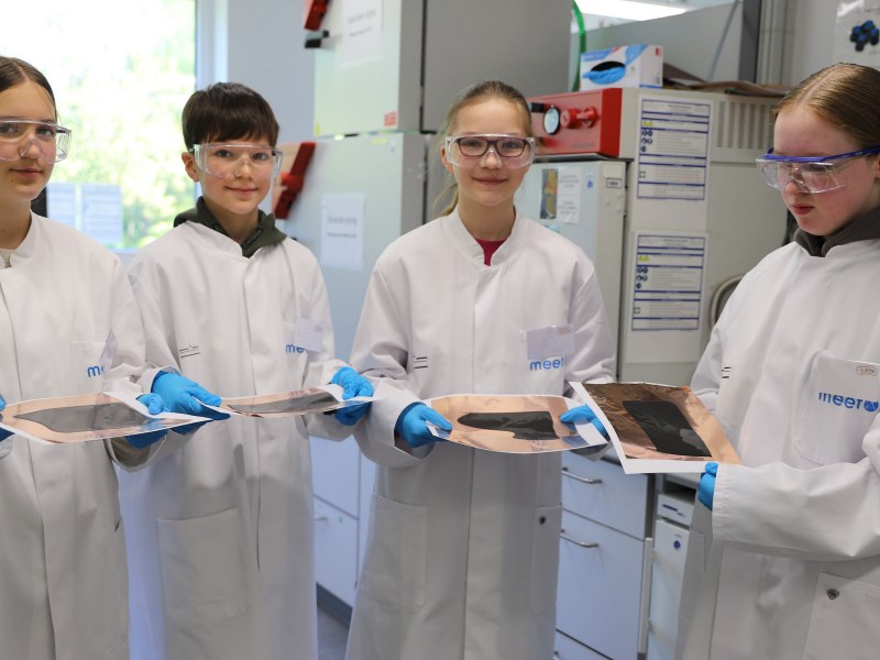 Vier Schülerinnen und Schüler tragen weiße Kittel und Schutzbrillen